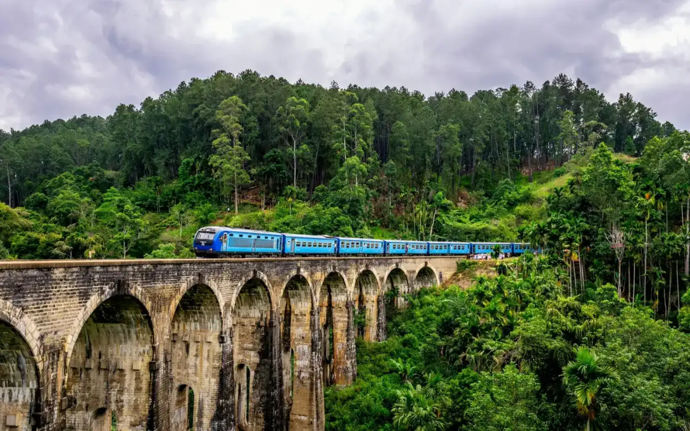 A blue train crossing the stone Nine Arches Bridge near Ella, with jungle and tea on both sides