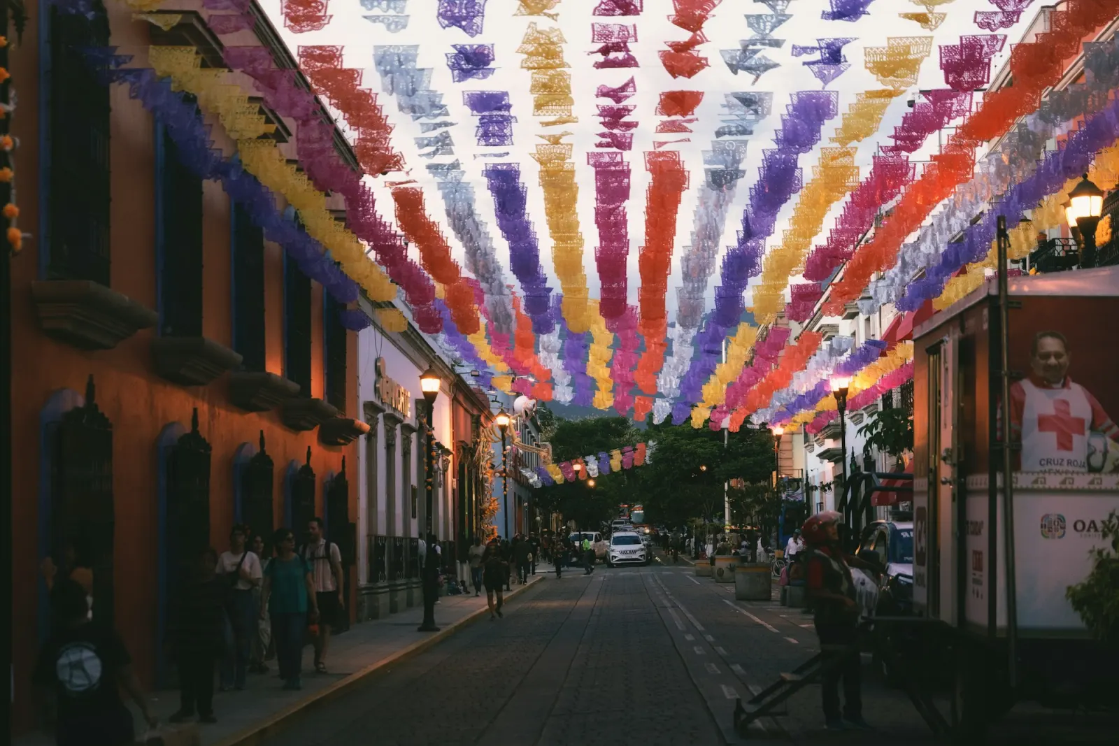 Strings of coloured papel picado banners across a street in Oaxaca at dusk, old buildings on both sides