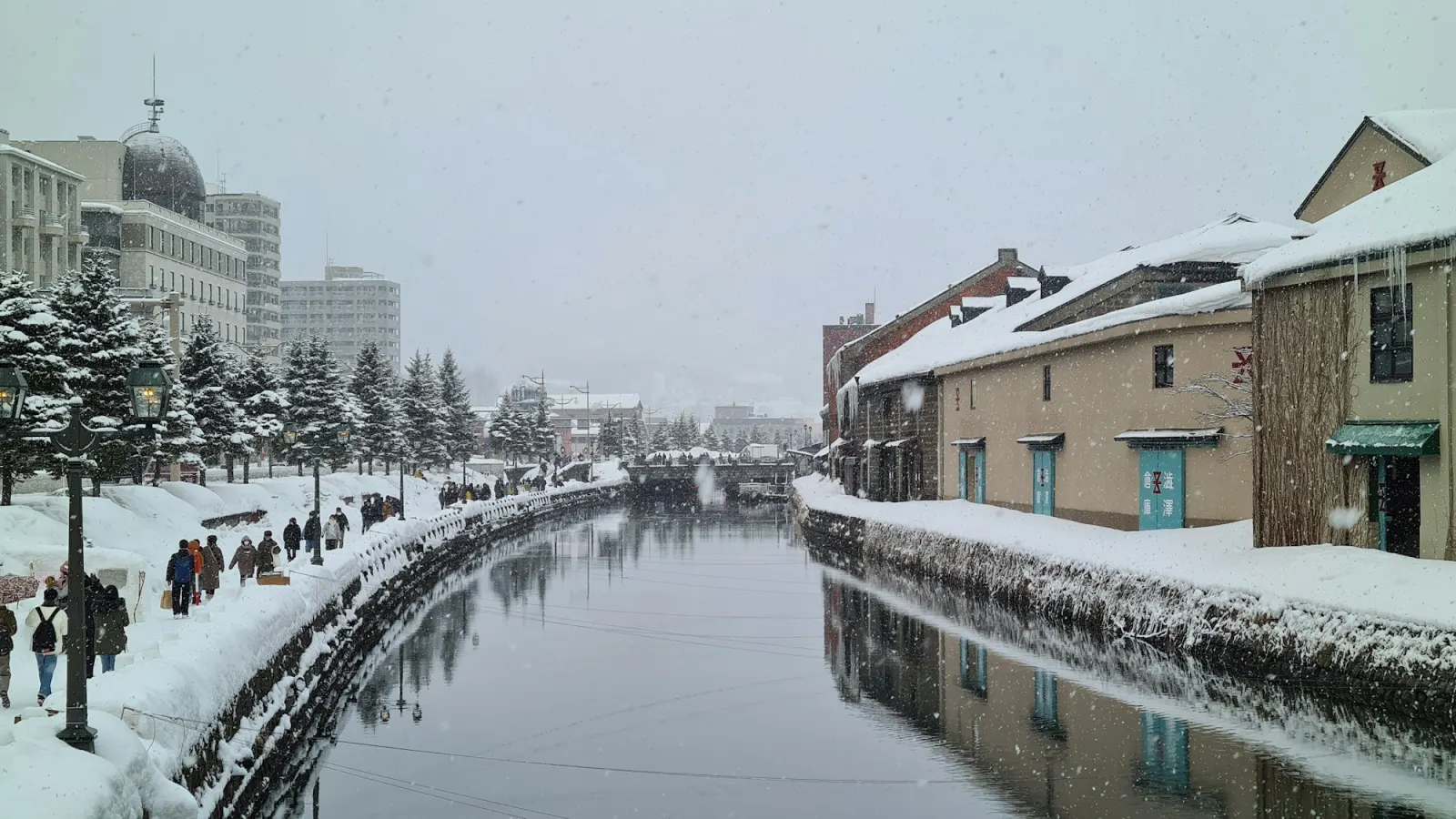 Otaru's canal in winter, snow on the stone banks and old warehouses lit along the water