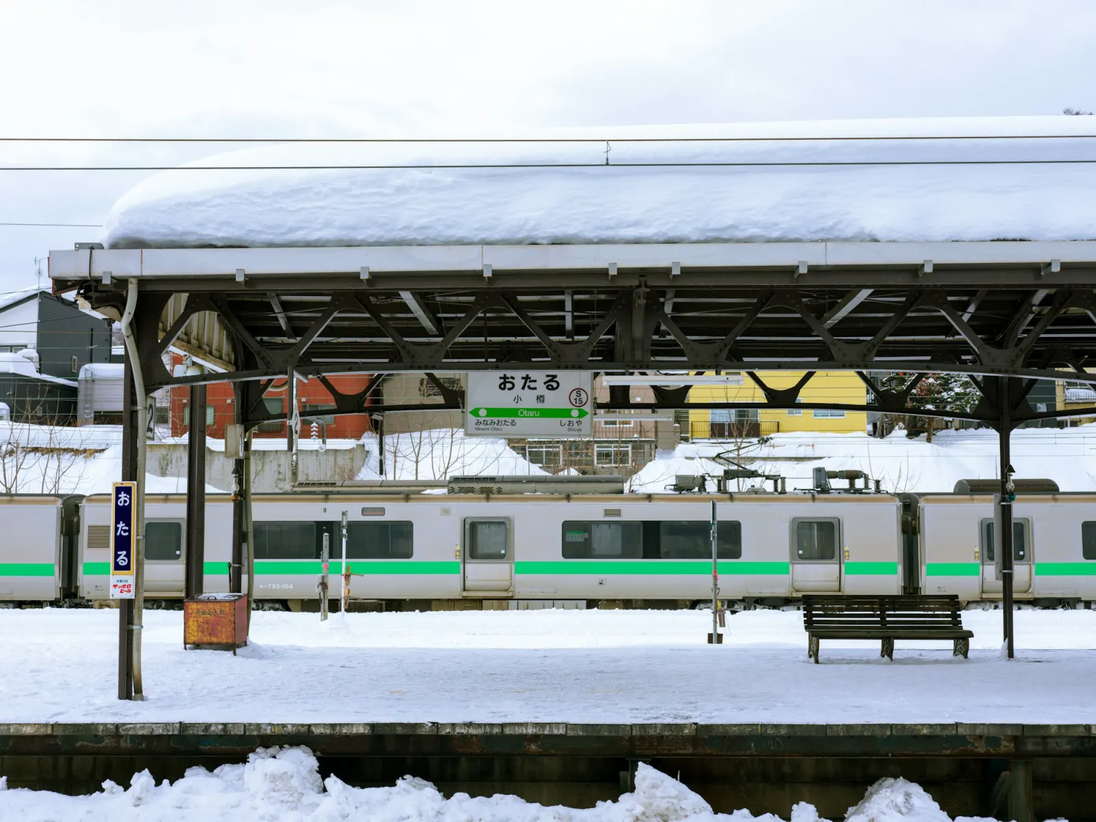 A small Hokkaido railway station buried in snow, with a train stopped at the platform
