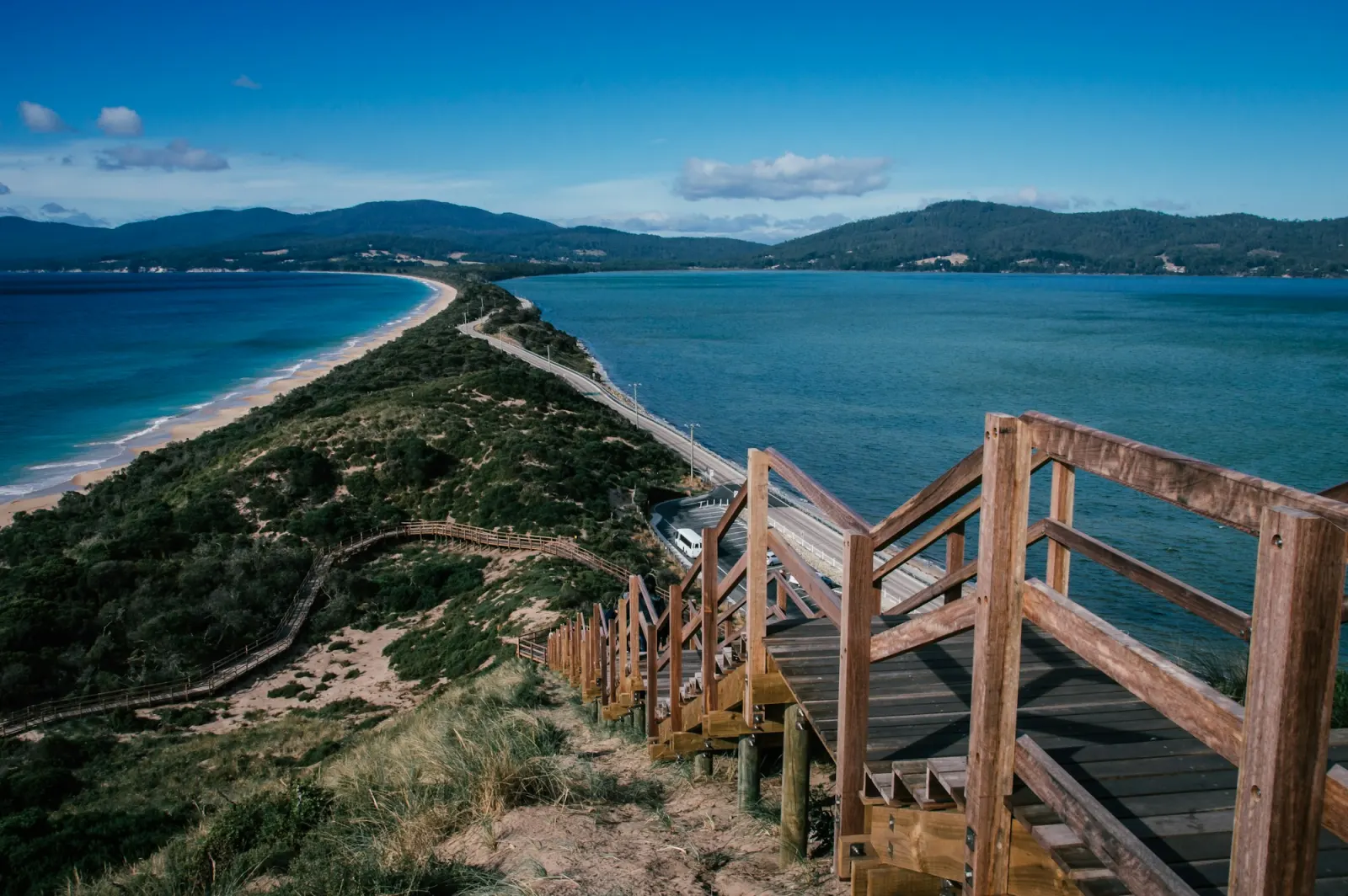 A timber boardwalk and steps climbing the dune at the Neck on Bruny Island, blue water either side