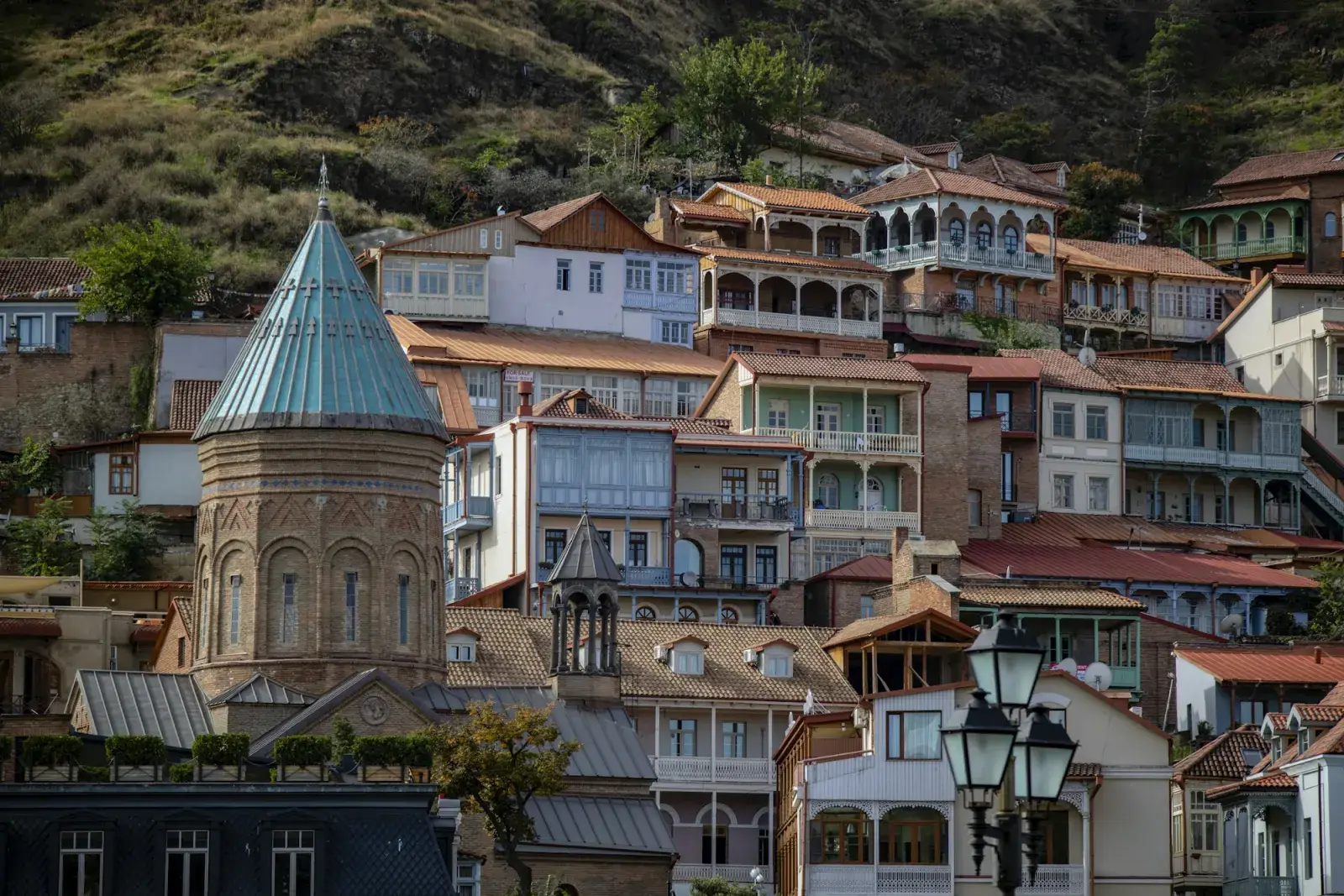 Old houses with wooden balconies stacked up a hillside in Tbilisi, a church dome above them