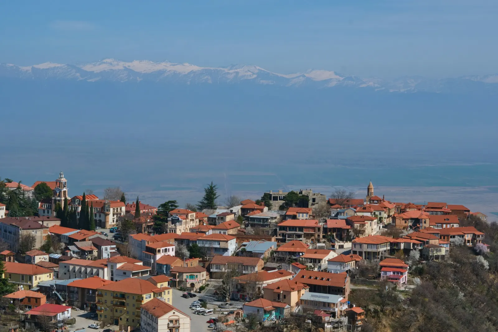 A small Georgian village with tiled roofs in front of a wall of mountains